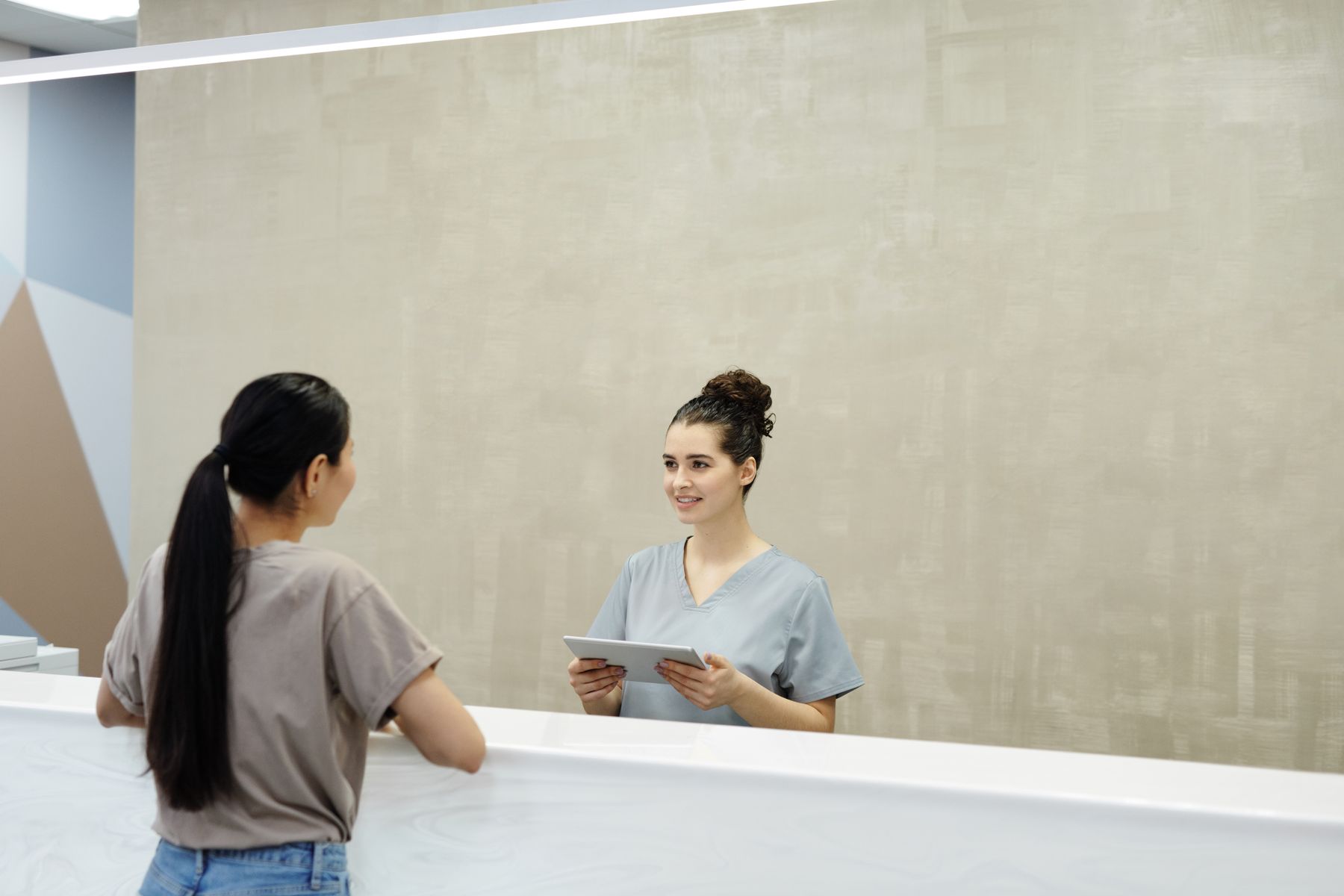 A friendly receptionist with a tablet greeting a patient at the front desk